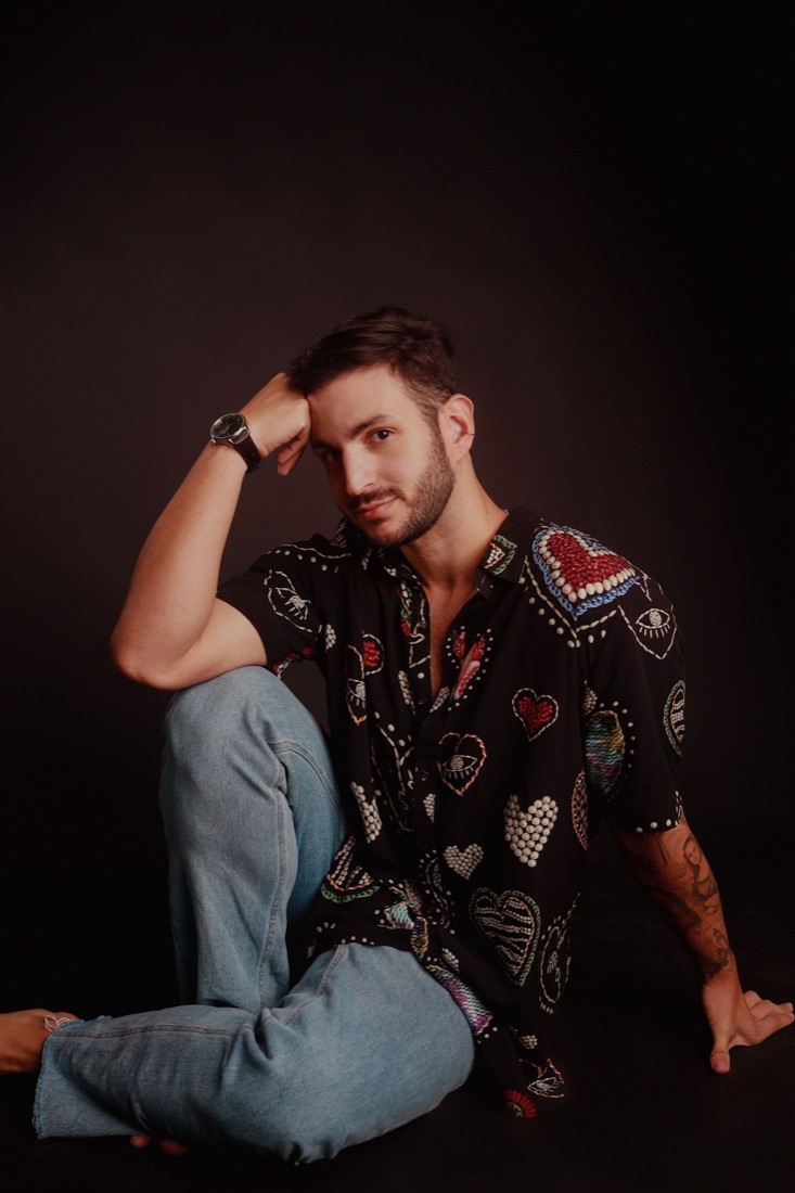 Homem sentado de camisa estampada, fundo escuro